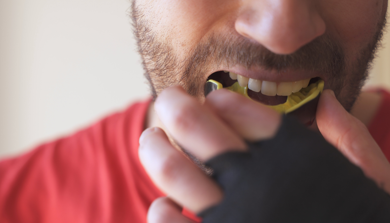 mouthguards-birkdale Close-up of a man biting into a yellow dental mouthguard held in his mouth.